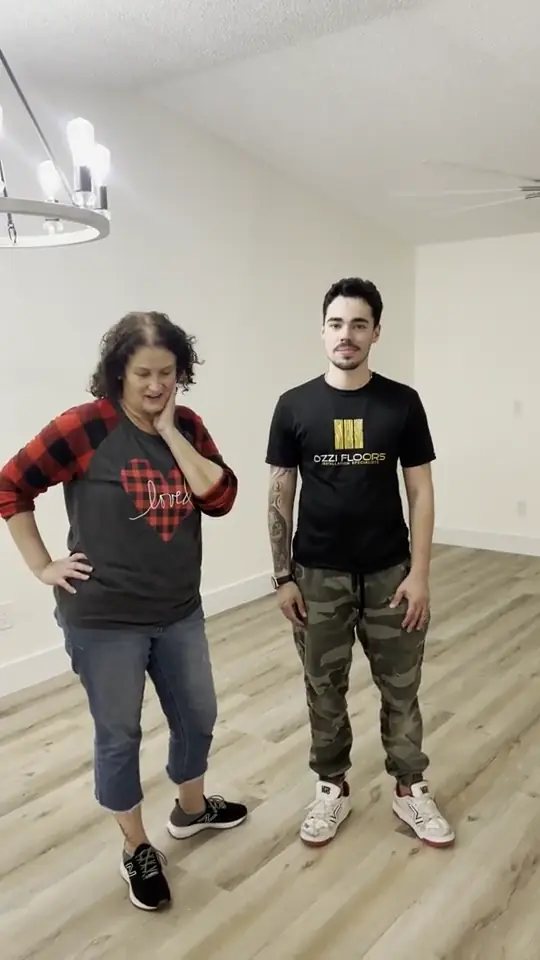An Ozzifloors team member standing with a customer in an empty room on her newly installed light grey plank floor