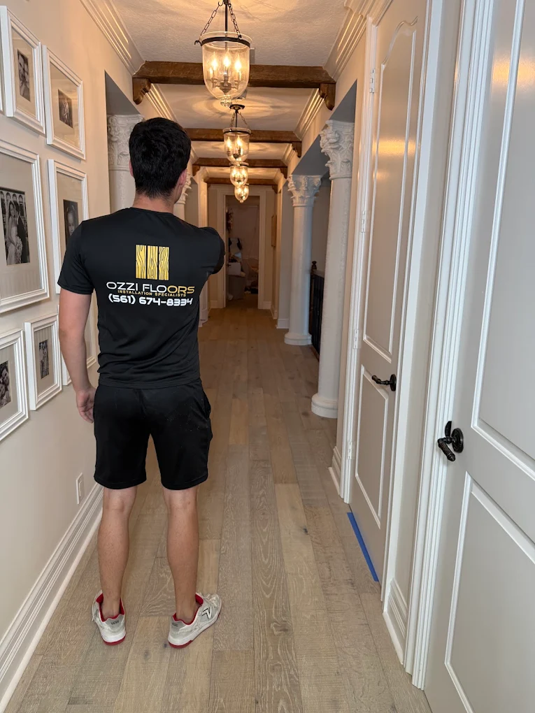 An Ozzifloors team member walking a finished hallway of light plank flooring, painter's tape still on the floor by a door