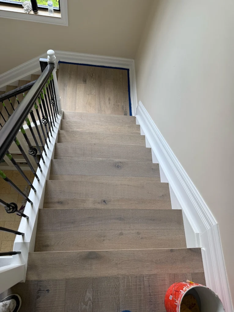 A staircase with new light plank treads and risers and an iron balustrade, painter's tape still down on the landing above