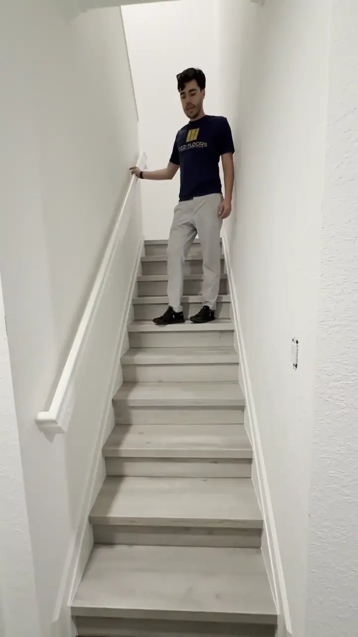 An Ozzifloors team member standing on a staircase wrapped in Plata Oak vinyl plank from CPF Floors, part of a Hollywood job with 14 steps